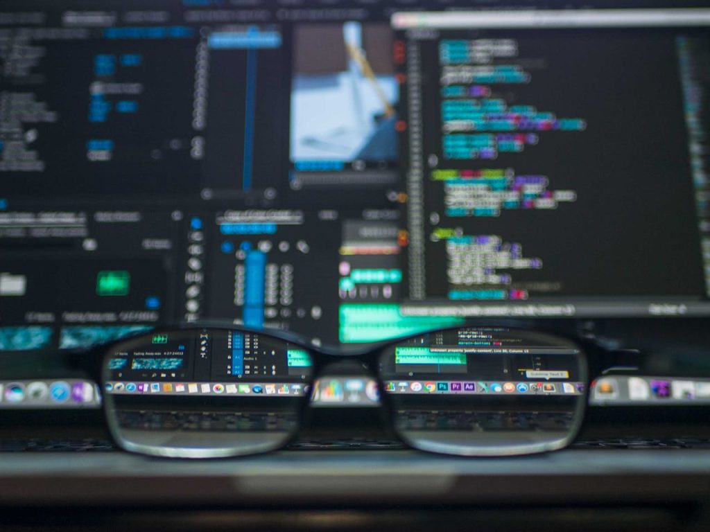 L'immagine un po' scura ritrae dei computer in cui scorrono dei dati e davanti ha un paio di occhiali